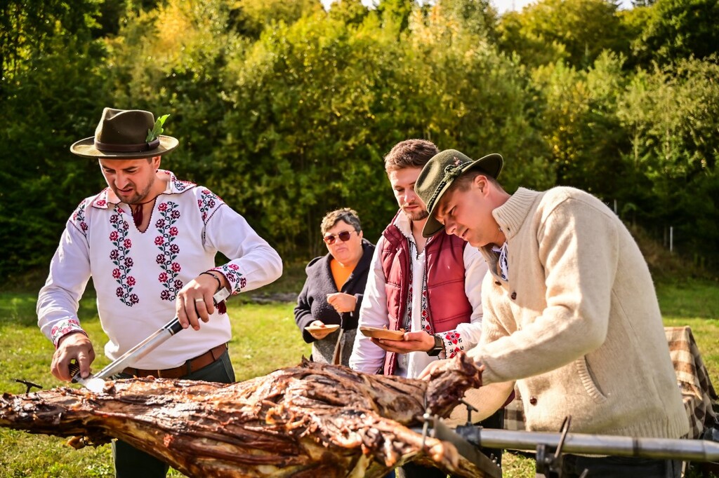 Trei bărbați în port popular taie o friptură mare la un târg gastronomic